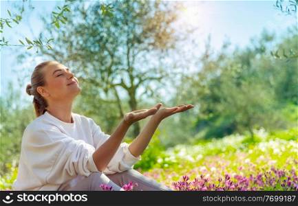 Nice happy woman sitting on flowers meadow in the garden, enjoying bright spring sunshine, active spring holidays in countryside