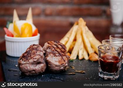 Nice peices of beef tenderloin steak with freach fried potatoes and various sauce on black stone plate