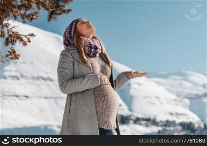 Nice Pregnant Woman With Closed Eyes of Pleasure Enjoying Bright Sun Light in Snowy Mountains. Spending Pregnancy Time in Winter Mountainous Resort.. Happy Pregnant Woman Enjoying Winter