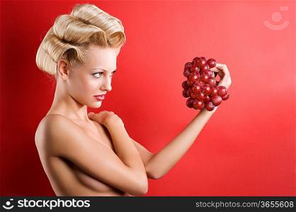 nice shot of Beautiful naked blond woman over red background looking a red grape