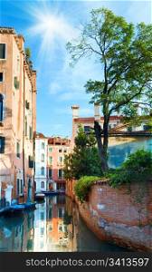 Nice summer venetian canal view with tree, sunshine in blue sky, and reflections (Venice, Italy)