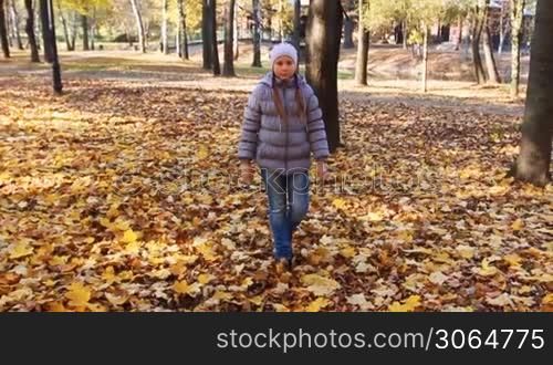 nice teen girl goes on yellow leaves in beautiful autumn city park, slow motion