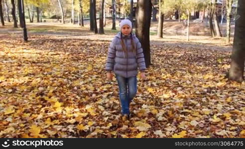 nice teen girl goes on yellow leaves in beautiful autumn city park, slow motion