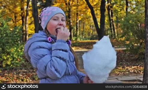 nice teen girl pecks off pieces cotton candy and eats in beautiful autumn city park, closeup