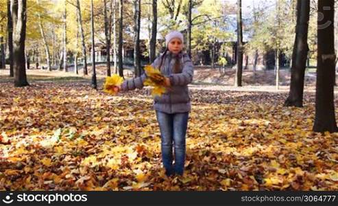 nice teen girl rotates and scatters yellow leaves in beautiful autumn city park
