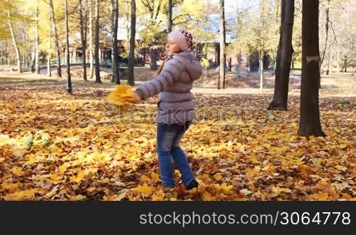 nice teen girl rotates with yellow leaves in her hands at beautiful autumn city park, slow motion