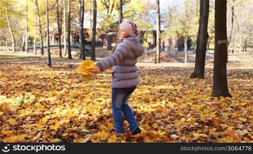 nice teen girl rotates with yellow leaves in her hands at beautiful autumn city park, slow motion
