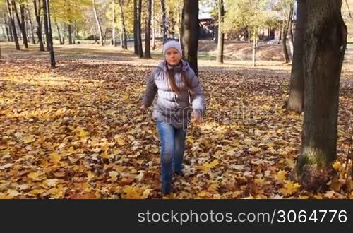 nice teen girl runs on yellow leaves in beautiful autumn city park, slow motion