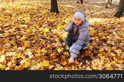 nice teen girl sits squatted and collects yellow leaves in beautiful autumn city park