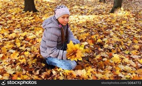 nice teen girl sits squatted and holds yellow leaves in beautiful autumn city park, then tosses up it