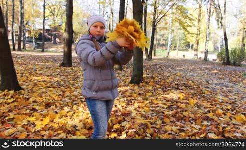 nice teen girl stands and scatters yellow leaves in beautiful autumn city park
