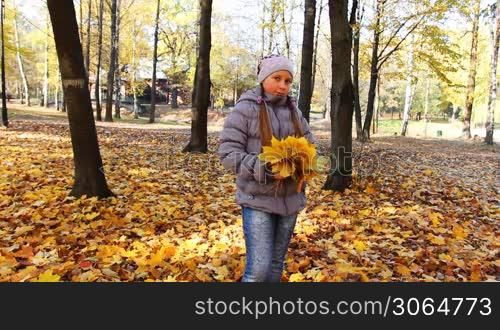 nice teen girl stands with yellow leaves in beautiful autumn city park, then tosses up it and goes away