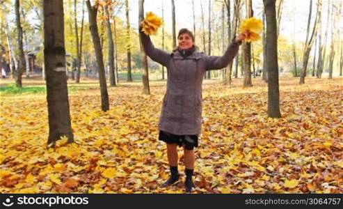 nice woman rotates and scatters yellow leaves in beautiful autumn city park