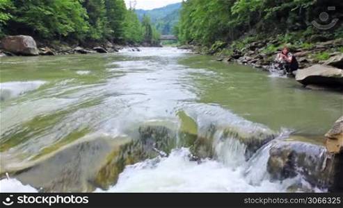 nice woman sits and plays with water on shore of river in mountains