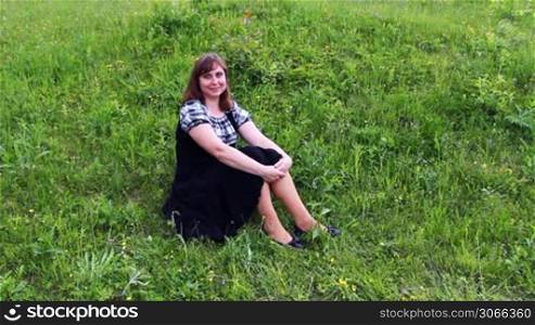 nice woman sits and smiles on grass at hillside