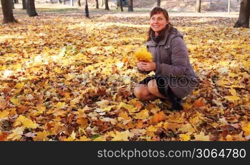 nice woman sits squatted, to her approaches teen daughter and they collect yellow leaves in beautiful autumn city park