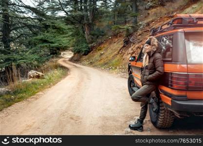 Nice woman standing near the SUV in the mountainous road, traveling along mountains by car, enjoying life and freedom