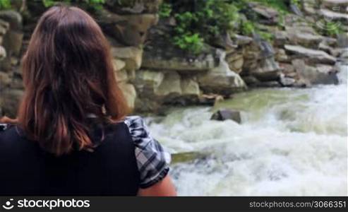 nice woman stands back and looks on waterfall, closeup