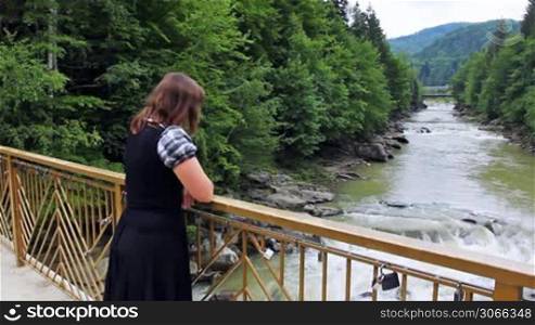 nice woman stands near railing bridge and looks on waterfall in Carpathian Mountains