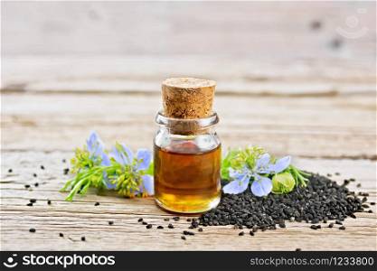 Nigella sativa oil in a bottle, seeds and twigs of black caraway seeds with blue flowers and green leaves of kalingi on a wooden board background