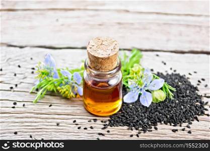 Nigella sativa oil in a bottle, seeds and twigs of black caraway seeds with blue flowers and green leaves on a background of an old wooden board