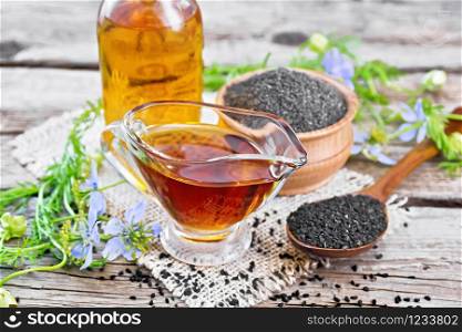 Nigella sativa oil in sauceboat and bottle, seeds in a spoon and black cumin flour in a bowl on burlap, kalingi twigs with blue flowers and green leaves on wooden board background