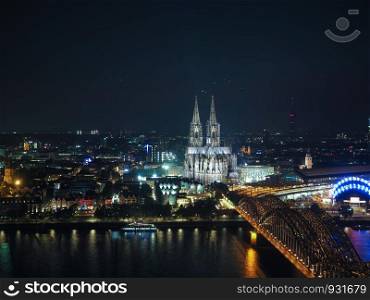Night aerial view Koelner Dom Sankt Petrus (meaning St Peter Cathedral) gothic church and Hohenzollernbruecke (meaning Hohenzollern Bridge) crossing the river Rhein in Koeln, Germany. Aerial night view of St Peter Cathedral and Hohenzollern Bridge over river Rhine in Koeln