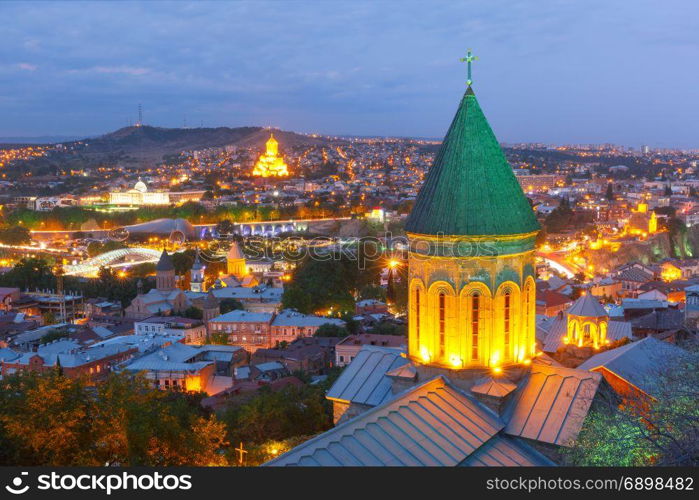 Night aerial view of Old Town, Tbilisi, Georgia. Aerial view of Old Town with dome of Lower Bethlemi Church and Sameba Holy Trinity Cathedral, Metekhi Church, bridge of Peace and Presidential Palace in night Illumination during evening blue hour, Tbilisi, Georgia.