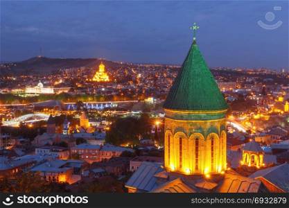Night aerial view of Old Town, Tbilisi, Georgia. Aerial view of Old Town with dome of Lower Bethlemi Church and Sameba Holy Trinity Cathedral, Metekhi Church, bridge of Peace and Presidential Palace in night Illumination during evening blue hour, Tbilisi, Georgia.