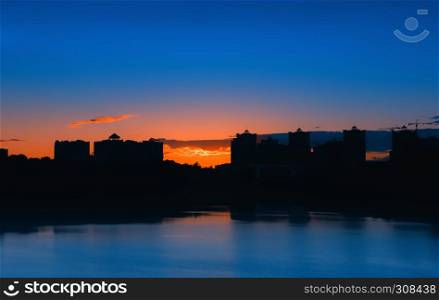 Night city landscape - silhouettes of high-rise buildings against the background of an sunset reflected in the lake.. Night City Landscape With Lake