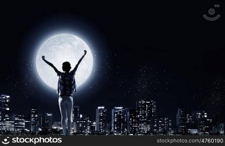 Night city life. Rear view of young woman with hands up looking at night city