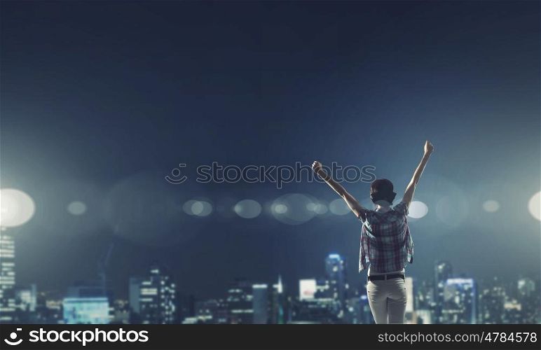 Night city life. Rear view of young woman with hands up looking at night city