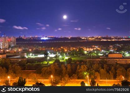 Night city panorama with urban landscape and illuminated buildings under moon and night sky. Kiev