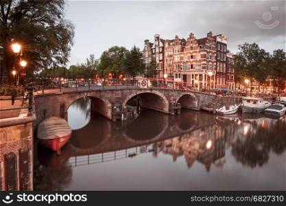 Night city view of Amsterdam canal and bridge. Amsterdam canal, bridge and typical houses, boats and bicycles during evening twilight blue hour, Holland, Netherlands. Used toning