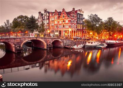Night city view of Amsterdam canal and bridge. Amsterdam canal, bridge and typical houses, boats and bicycles during evening twilight blue hour, Holland, Netherlands. Used toning