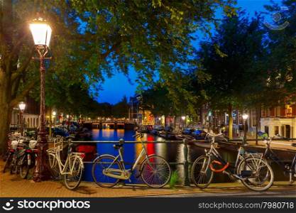 Night city view of Amsterdam canal and bridge, boats and bicycles, Holland, Netherlands.
