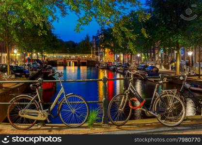 Night city view of Amsterdam canal and bridge, boats and bicycles, Holland, Netherlands.