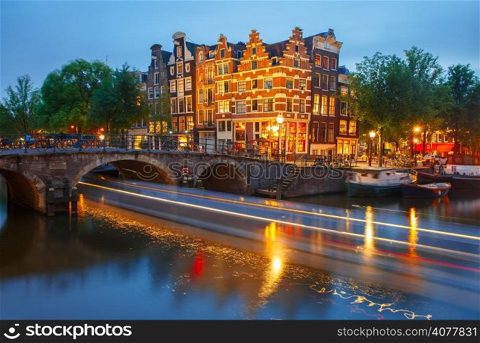 Night city view of Amsterdam canal, bridge and typical houses, boats and bicycles, Holland, Netherlands.