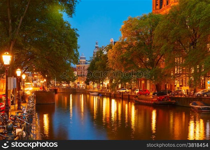 Night city view of Amsterdam canal, bridge, boats and bicycles, Holland, Netherlands.