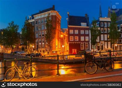 Night city view of Amsterdam canal, bridge, typical houses and bicycles, Holland, Netherlands.