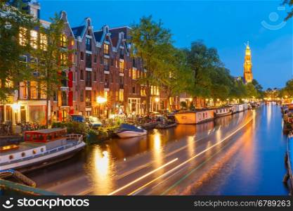Night city view of Amsterdam canal Prinsengracht with houseboats and Westerkerk church and luminous track from the boat, Holland, Netherlands.