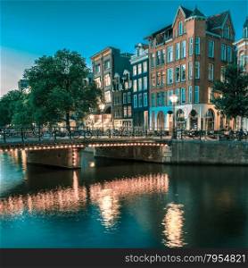 Night city view of Amsterdam canal, typical dutch houses and bridge, Holland, Netherlands.. Toning in cool tones