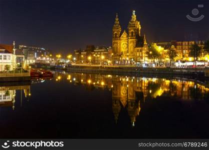 Night city view of Amsterdam canal with Basilica of Saint Nicholas and its mirror reflection in the water, Holland, Netherlands. Long exposure.