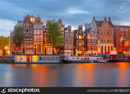 Night city view of Amsterdam canal with dutch houses. Amsterdam canal Amstel with typical dutch houses and boats during twilight blue hour, Holland, Netherlands.