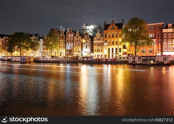 Night city view of Amsterdam canal with dutch houses. Amsterdam canal Amstel with typical dutch houses, houseboat and luminous track from the boat at night, Holland, Netherlands.
