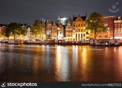 Night city view of Amsterdam canal with dutch houses. Amsterdam canal Amstel with typical dutch houses, houseboat and luminous track from the boat at night, Holland, Netherlands.