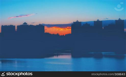 Night cityscape background - silhouettes of high rise buildings against the sunset reflected in the lake.. Night Sunset Cityscape Background