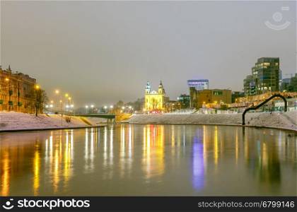 Night cityscape of the Neris River, Church and skyscrapers in the center of Vilnius at sunset. Lithuania.