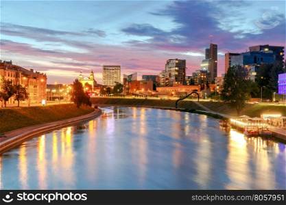 Night cityscape of the Neris River, Church and skyscrapers in the center of Vilnius at sunset. Lithuania.
