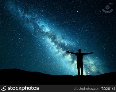 Night colorful landscape with green Milky Way and silhouette of a happy man with raised up arms on the hill. Beautiful Universe. Travel background with starry sky.
